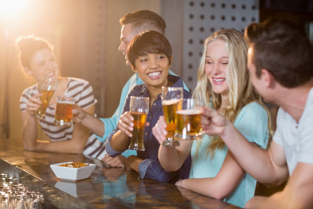 Group of smiling friends toasting glass of beer at counter in bar