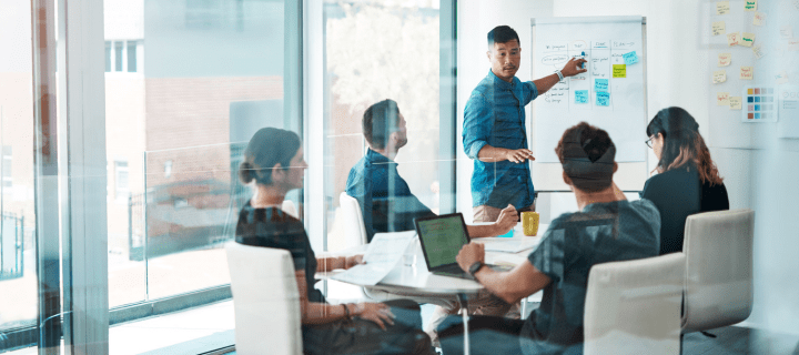 Man at white board giving presentation to a team in a conference room.